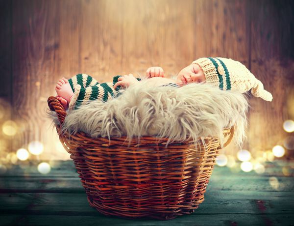 نوزاد دو هفته ای با لباس بافتنی خنده دار که در یک سبد روی پس زمینه چوبی می خوابد عکس استودیویی پرتره نوزاد شیرین روی پس‌زمینه روستایی چوبی پسر تازه متولد شده
