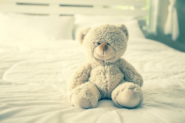 خرس عروسکی با افسردگی نشسته روی تخت تن رنگی قدیمی