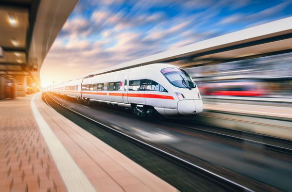 قطار پرسرعت سفید مدرن در حال حرکت در ایستگاه راه آهن در غروب آفتاب قطار در مسیر راه آهن با جلوه حرکت تاری در اروپا در عصر سکوی راه آهن چشم انداز صنعتی گردشگری راه آهن