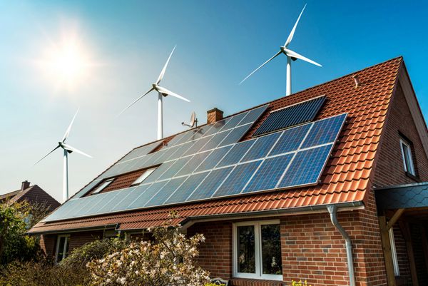 پنل خورشیدی روی سقف خانه و توربین های بادی در اطراف - مفهوم منابع پایدار