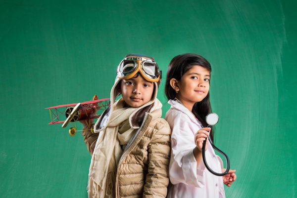 مفهوم کودکان و آموزش - پسر و دختر هندی کوچکی که در مقابل تخته گچی سبز با لباس فانتزی مهندسین و لباس پزشک با گوشی پزشکی می‌خواهم مهندس یا دکتر باشم ژست می‌گیرند