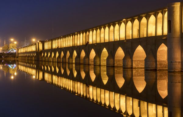 اصفهان ایران - 18 فوریه 2016 نمایی شبانه از پل نورانی سه‌وسه پل 33 طاق که در زاینده رود منعکس شده است چند نفر روی پل قابل مشاهده هستند