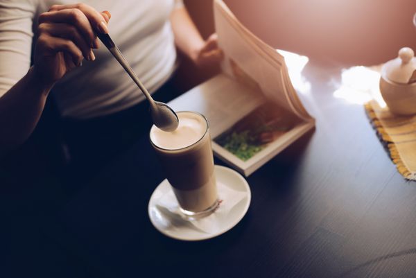 مشتری زن کافه که کافه لاته را با قاشق مخلوط می کند و کتاب می خواند