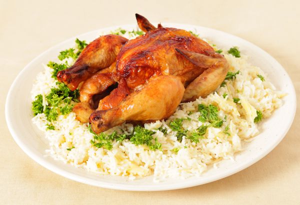نمایی با زاویه بالا از مرغ سوخاری روی تختی از برنج پخته شده تزئین شده با جعفری
