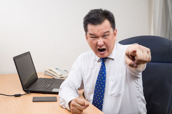 مدیر آسیایی عصبانی و پراسترس در حال فریاد زدن و اشاره در دفتر