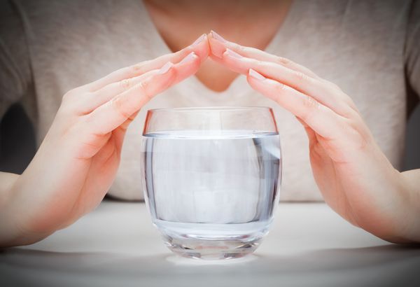 یک لیوان آب معدنی تمیز که با دستان زن پوشیده شده است حفاظت از محیط زیست