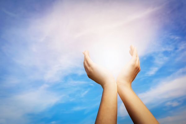 دستان بلند شده در حال گرفتن خورشید در آسمان آبی مفهوم معنویت