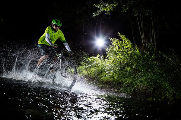 دوچرخه سوار کوهستانی که با سرعت در حال عبور از رودخانه جنگلی است پاشش آب در حرکت انجماد