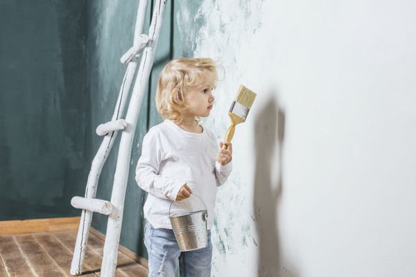کودک زیبا و شاد کوچک با شلوار جین دیوار را با br نقاشی می کند