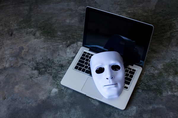 ماسک ناشناس برای پنهان کردن هویت در لپ‌تاپ کامپیوتر - مفهوم تهدید امنیت اینترنتی و جنایتکارانه اینترنتی