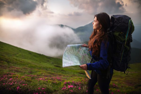 تصویری از زن جوانی که نقشه ای در دست دارد در حالی که منظره ای را از بالای کوه می گیرد