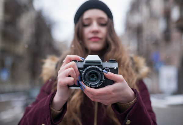 عکاس دختر هیپستر با دوربین رترو که در خیابان شهر عکس می گیرد