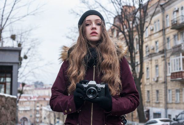 عکاس دختر هیپستر با دوربین رترو که در حال قدم زدن در خیابان شهر عکس می گیرد