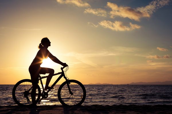 زن شاد با دوچرخه ایستاده در ساحل