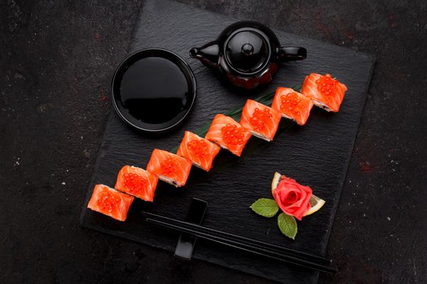 غذای ژاپنی سوشی ماهی قزل آلا روی یک صفحه سنگی روی پس زمینه بتنی رول می شود