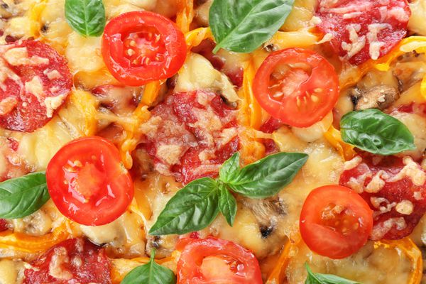 نمای نزدیک از پیتزای خوشمزه با پپرونی پنیر گوجه فرنگی ریحان و فلفل سالاد