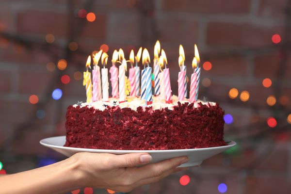 بشقاب دستی زن با کیک تولد خوشمزه در برابر نورهای غیر متمرکز