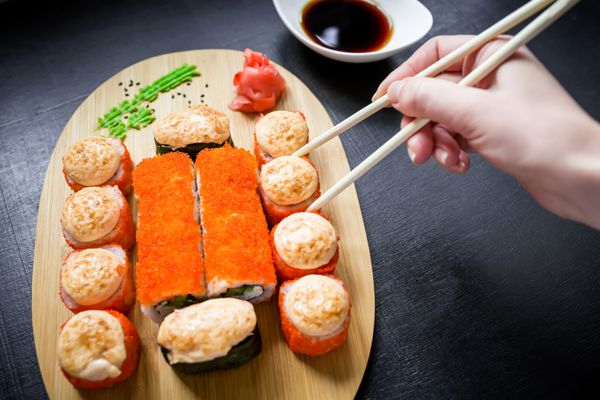 رول سوشی سس و دست زن روی پس‌زمینه سیاه غذای ژاپنی نمای بالا تخت دراز کشید