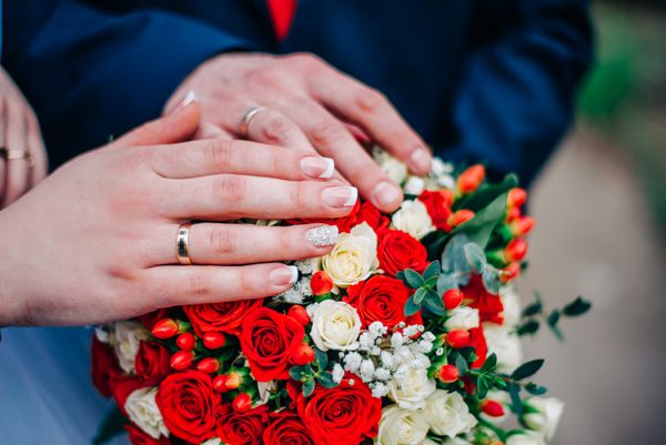 دستان یک زوج تازه ازدواج کرده روی دسته گل عروسی
