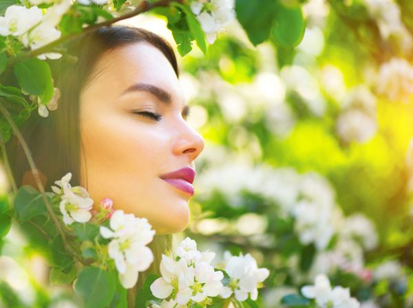 زن جوان زیبا در حال لذت بردن از طبیعت بهاری در درخت سیب شکوفه و خندان