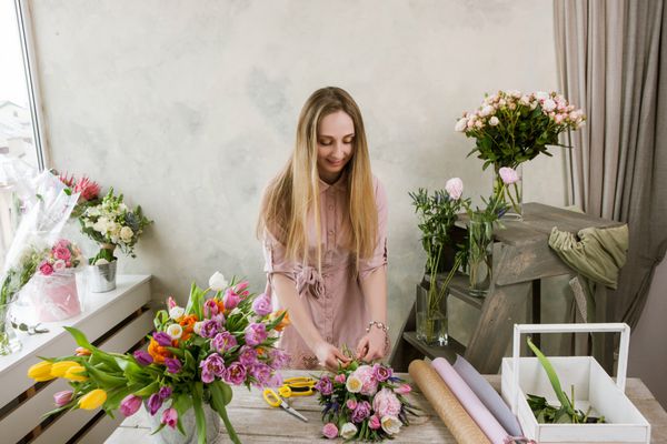 گلفروش در کارگاه یک دسته گل بسته بندی می کند کار دکوراتور با خلقت او زنی در گل فروشی که گل فروشی را جمع آوری می کند