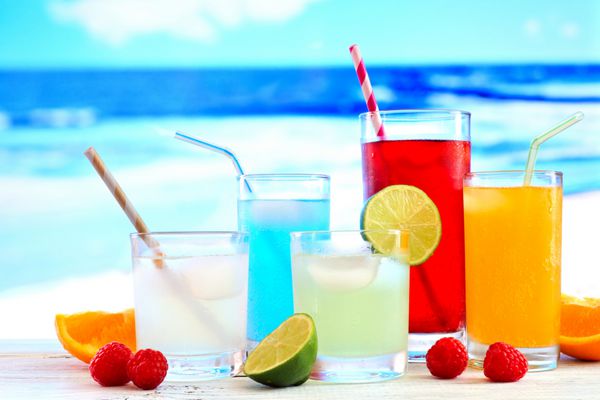 گروهی از نوشیدنی های رنگارنگ تابستانی در مقابل پس زمینه آبی پر جنب و جوش اقیانوس