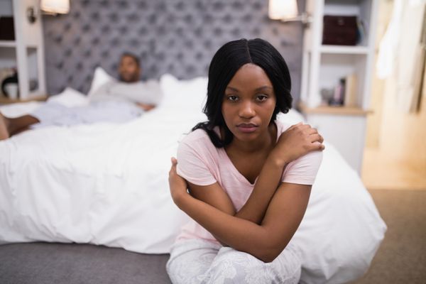 زن جوان نشسته در حالی که مرد روی تخت در خانه دراز کشیده است
