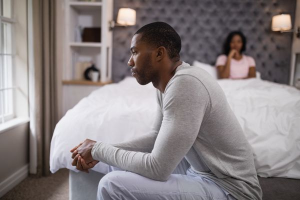 مرد جوانی نشسته در حالی که زن روی تخت در خانه استراحت می کند