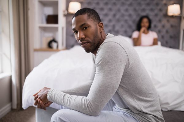 مرد جوانی نشسته در حالی که زن روی تخت در خانه استراحت می کند