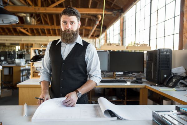 مرد حرفه ای مدرن در دفتر کار بزرگ با کاغذهای طراحی ایستاده است
