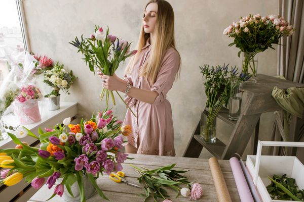 دکوراتور حرفه ای گل فروشی در گل فروشی دسته گل جدید را می سازد کار زن با مجموعه لاله محل کار هنرمند