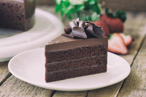 نانوایی خانگی کیک فاج شکلاتی تزئین شده با حلقه شکلاتی تکه مثلثی کیک شکلاتی روی میز چوبی روستایی برای کافه جلسه وقت استراحت قهوه یا چای و جشن تولد