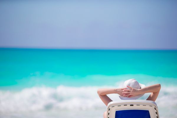 زن جوانی با کلاه در ساحل استوایی که به دریای زیبا نگاه می کند