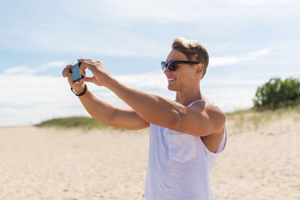 مردی با گوشی هوشمند در حال عکاسی در ساحل تابستانی