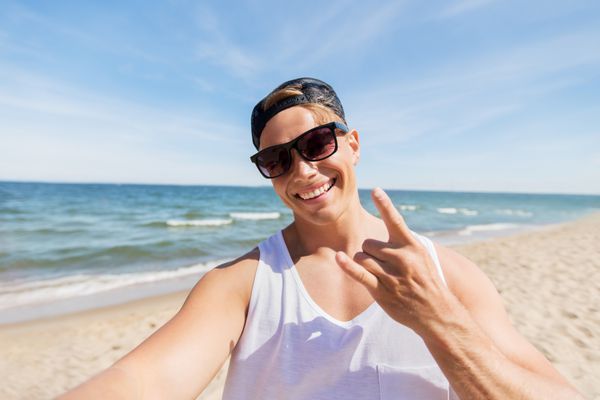 مردی با عینک آفتابی در حال گرفتن سلفی در ساحل تابستانی