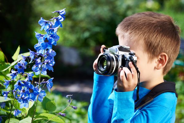 پسر بچه با دوربین رترو که از گل های ماکرو عکس می گیرد