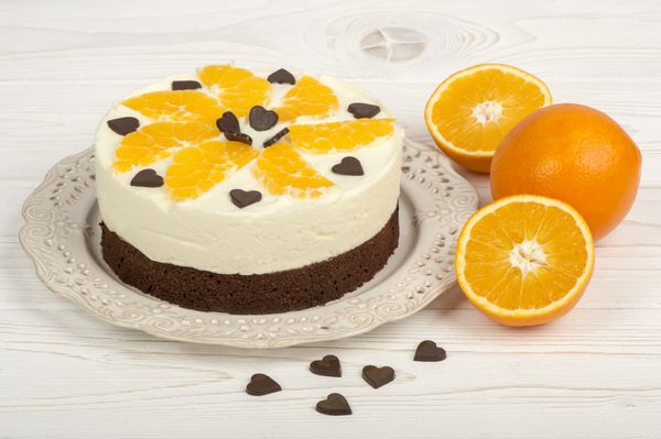 کیک براونی با خامه و پرتقال در زمینه چوبی سفید