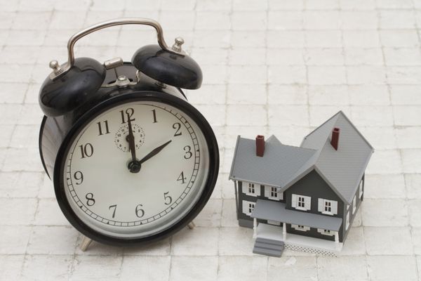 زمان خرید خانه خانه خاکستری و ساعت زنگ دار روی پشته سنگی