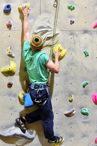 Mann klettert در einer Indoor-Kletterhalle die Wand hoch