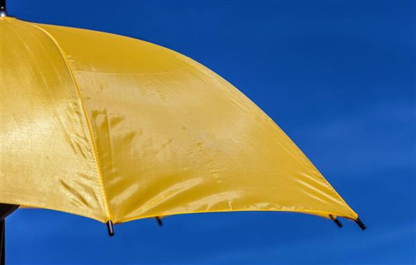 تصویر نزدیک از یک چتر زرد در برابر آفتاب