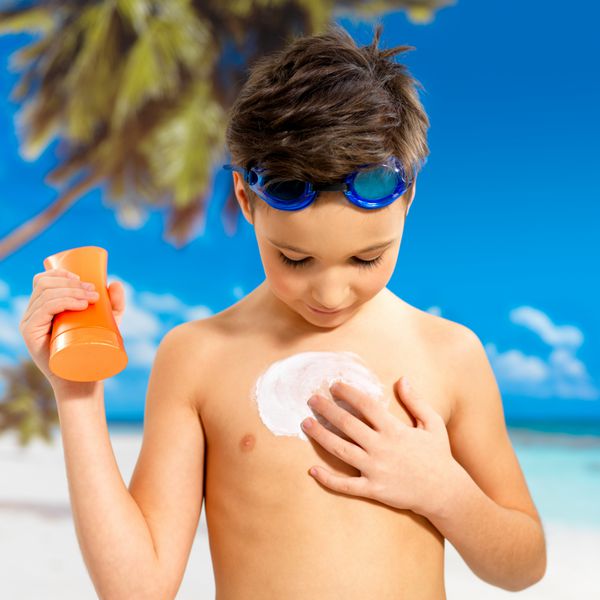 پسر schoolchild استفاده از کرم آفتاب بر روی بدن دباغی پسر برگزاری نارنجی خورشید برنزه شدن لوسیون بطری