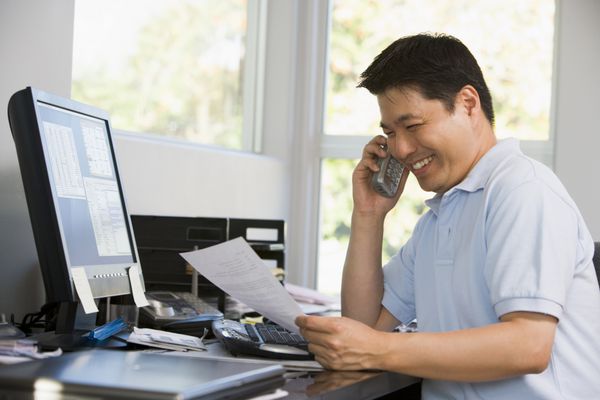 مرد در دفتر خانه با رایانه و کارهای کاغذی در تلفن لبخند می زند