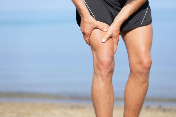آسیب عضلانی مرد با عضلات ران اسپری ورزشکار در شورت های ورزشی که از عضلات ران خود رانده می شود پس از کشیدن و یا تکان دادن آنها در حالی که دویدن در ساحل