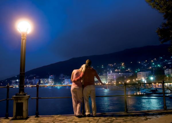 زن و شوهر ایستاده در نزدیکی دریا و به چشم انداز شبانه شهرستان چشم انداز