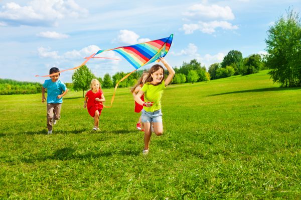چهار بچه کوچک در پارک با بادبادک شاد و لبخند می زنند