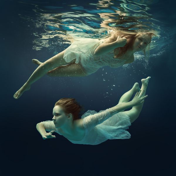 زن و دختر در لباس های زیبا در زیر آب شنا می کنند