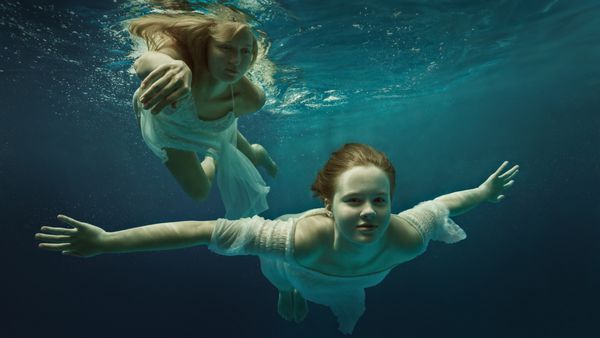 زن و دختر در لباس های زیبا در زیر آب شنا می کنند