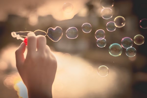 حباب قلب من در آسمان غروب آفتاب عشق در آفتاب تابستان با دمنده حباب عاشقانه حباب های صابون رنگارنگ در پارک