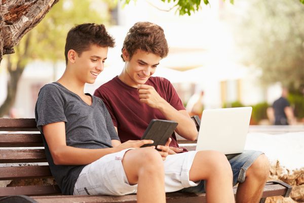 پسران نوجوان در پارک بنچ با استفاده از لپ تاپ و تبلت دیجیتال