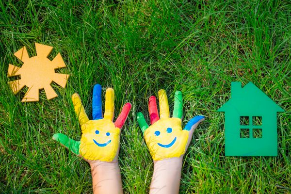 لبخند بر روی دست خانه کاغذ و خورشید در چمن سبز کودکان سرگرم کننده در بهار خارج از منزل هستند مفهوم اکولوژی